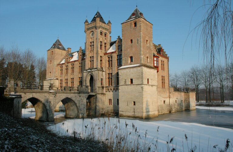 Scenic winter view of a historic castle in Brugge, Belgium with a partially frozen moat.