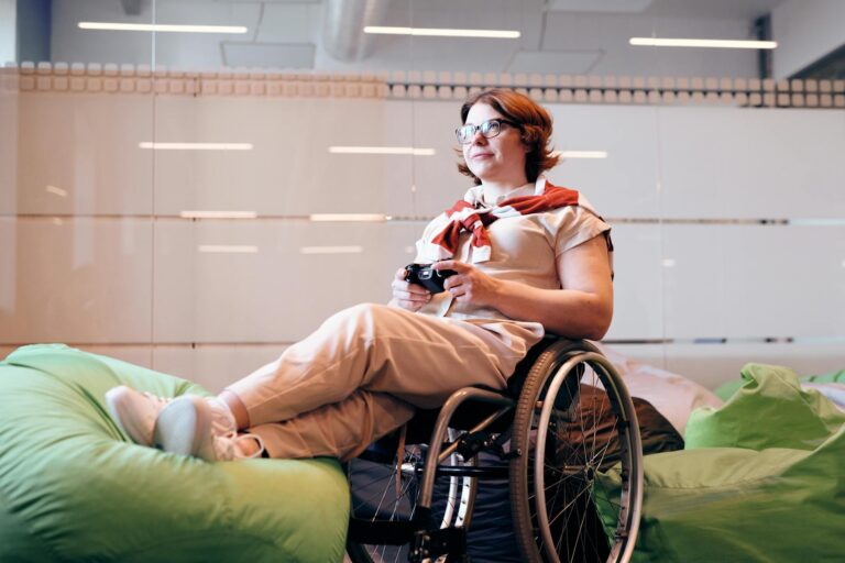 A woman in a wheelchair enjoys playing games indoors, holding a remote control.